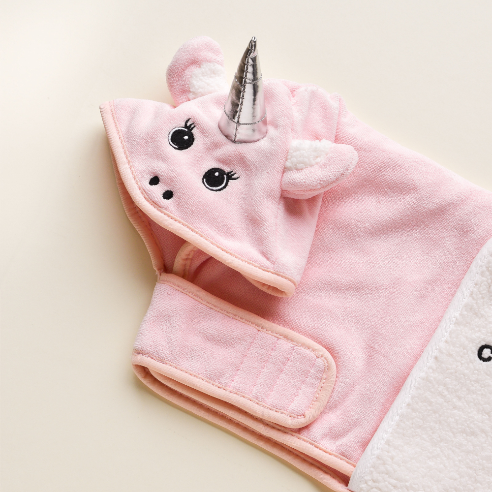 Introducing the PRE-ORDER Pupicorn Drying Robe by Cocopup London: a soft, pink baby blanket with an adorable unicorn-themed hood featuring embroidered eyes, ears, and a shiny silver horn. This charming robe includes convenient velcro straps for securing around your baby and is crafted from premium microfibre. The background is a versatile off-white.