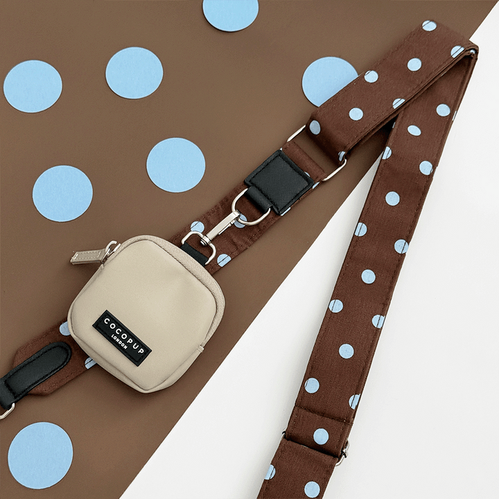 A brown bag strap with light blue polka dot design. Attached is a beige small pouch for dog treats.