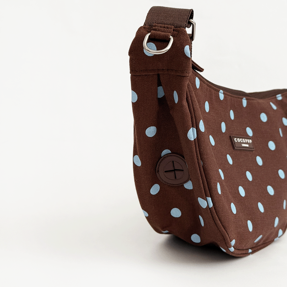 A brown fabric crossbody bag with a light blue polka dot pattern. Featuring Cocopup London logo badge and plain brown strap.