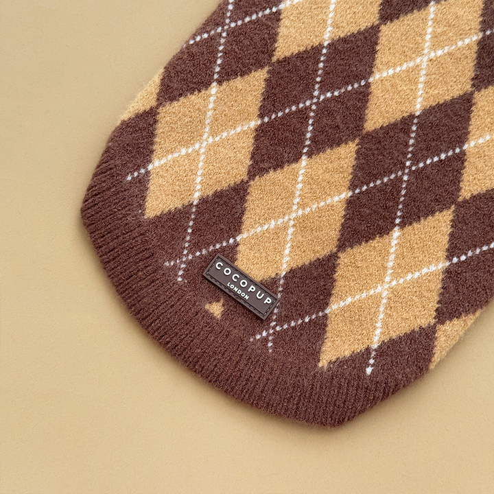 Close up of the bottom of a dog jumper in a brown, tan, and white argyle pattern. 