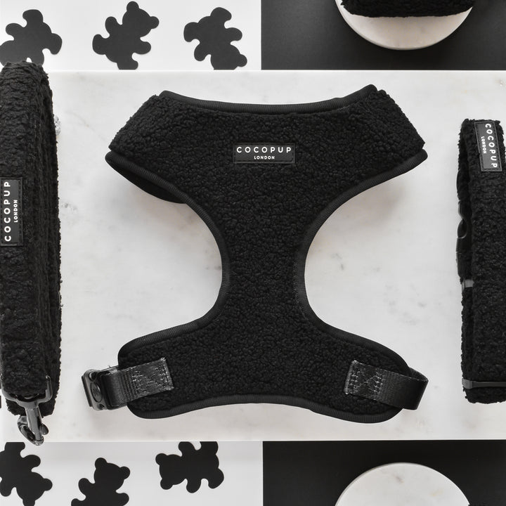 The Teddy Baloo Adjustable Neck Harness, Lead & Collar Bundle from Cocopup London is displayed on a white surface with black bone shapes in the background. The neoprene material of the harness features a fur-like texture and a buckle closure. Matching accessories, including an adjustable neck harness and dog collar, are laid alongside for a chic, coordinated look.