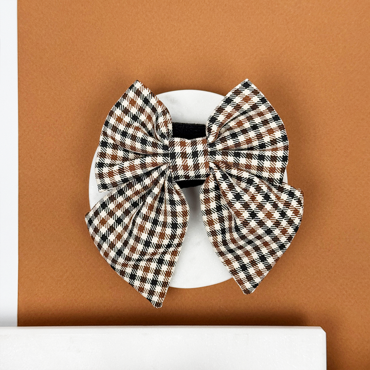 Beige, black, and brown checkered sailor bow tie displayed on a round white surface.