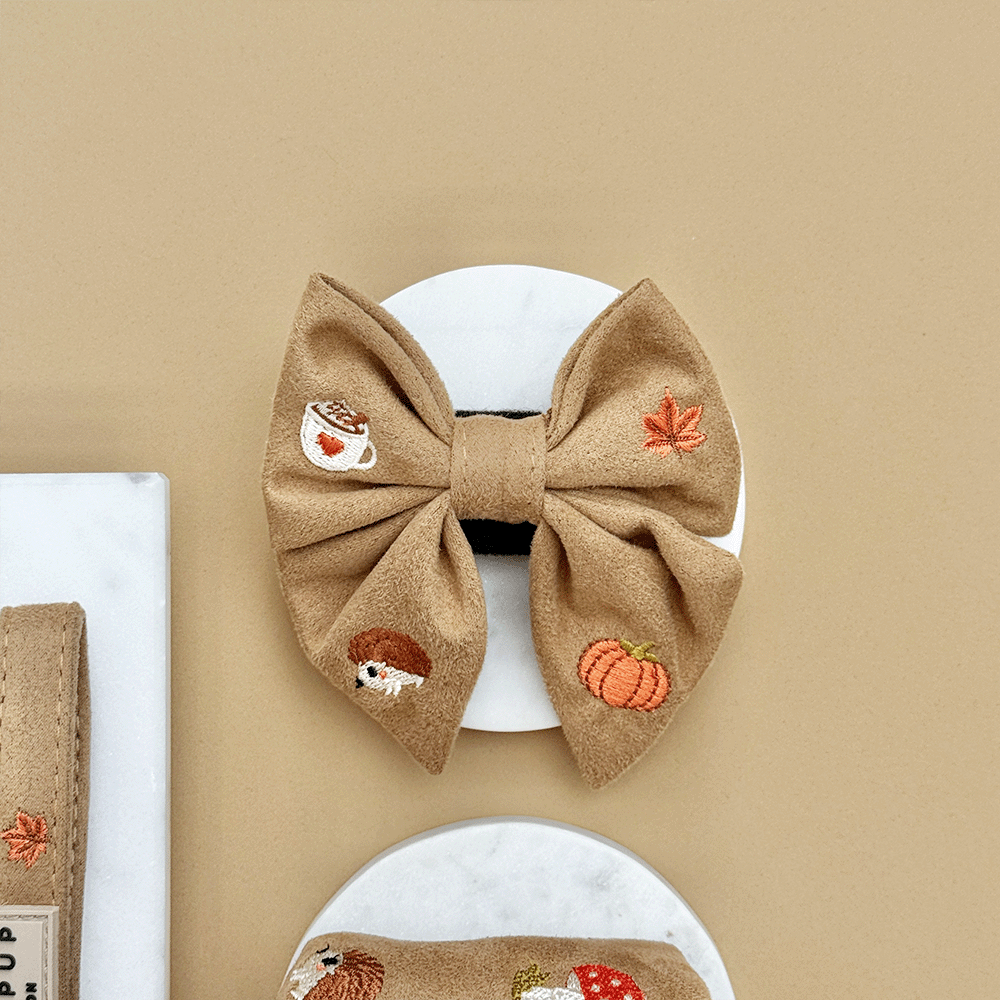 Brown dog sailor bow tie, with autumnal-themed embroidery of pumpkins, leaves, a coffee cup, and mushrooms.